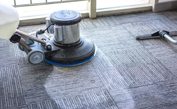 rotary floor scrubber cleaning gray patterned carpet.